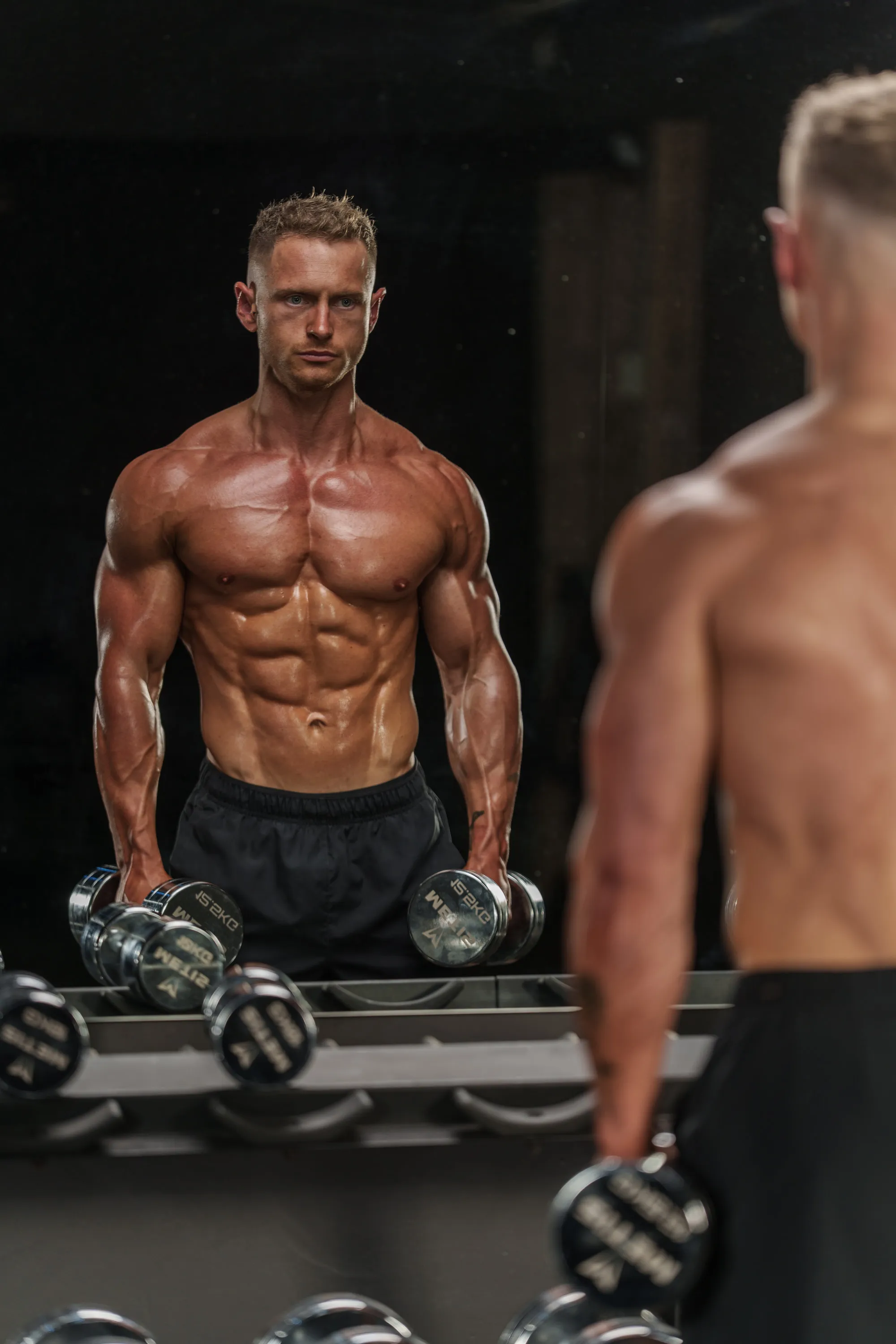 Callum holding a pair of dumbbells in front of a gym mirror