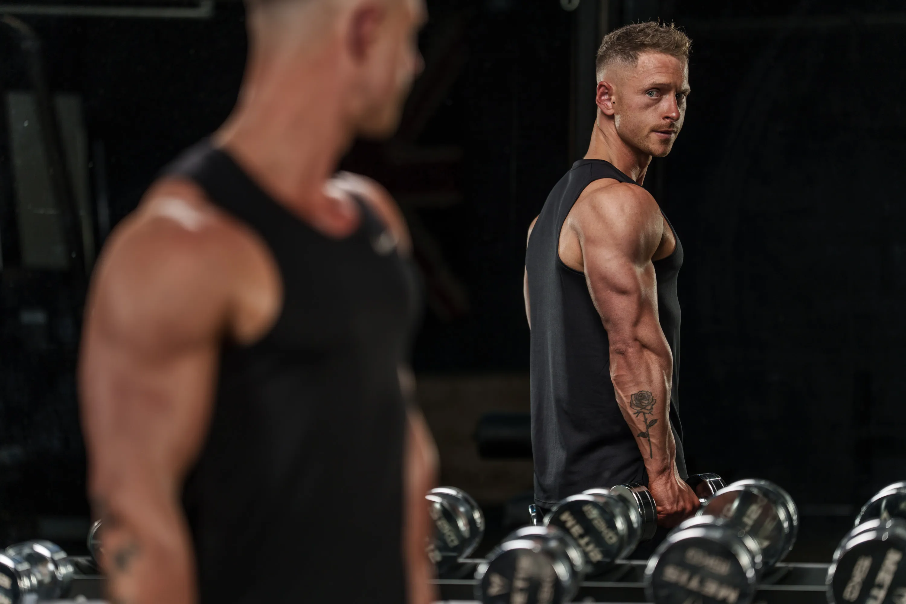 Callum in a tank top, side-on beside a squat rack